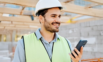 Mitarbeitender auf Baustelle mit Mitarbeiter-App am Smartphone